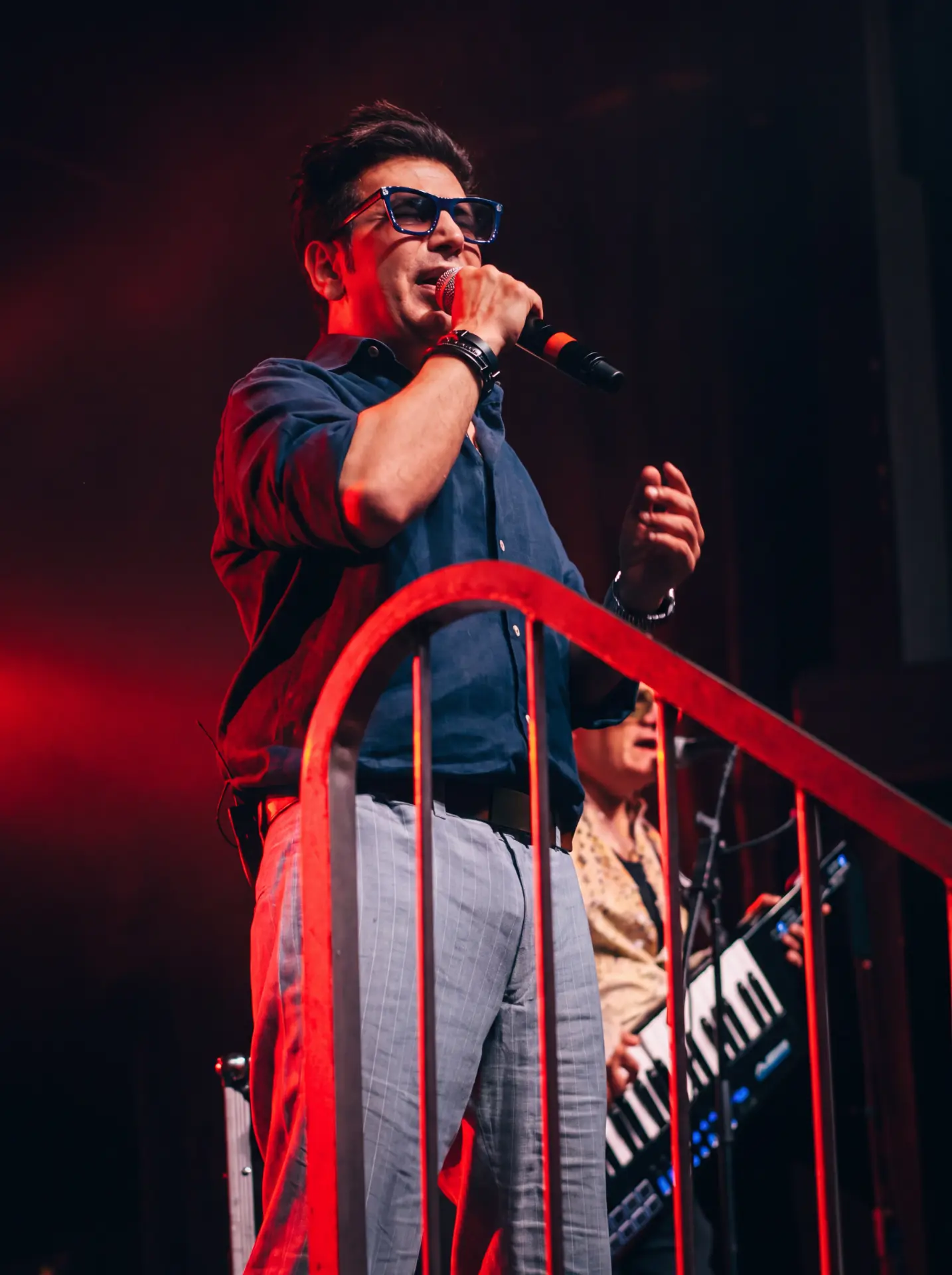 Singer in blue glasses performing under red stage lighting