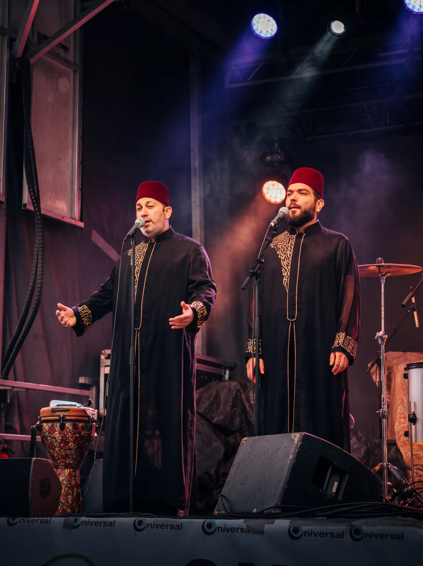 Two vocalists in traditional robes performing under purple stage lights