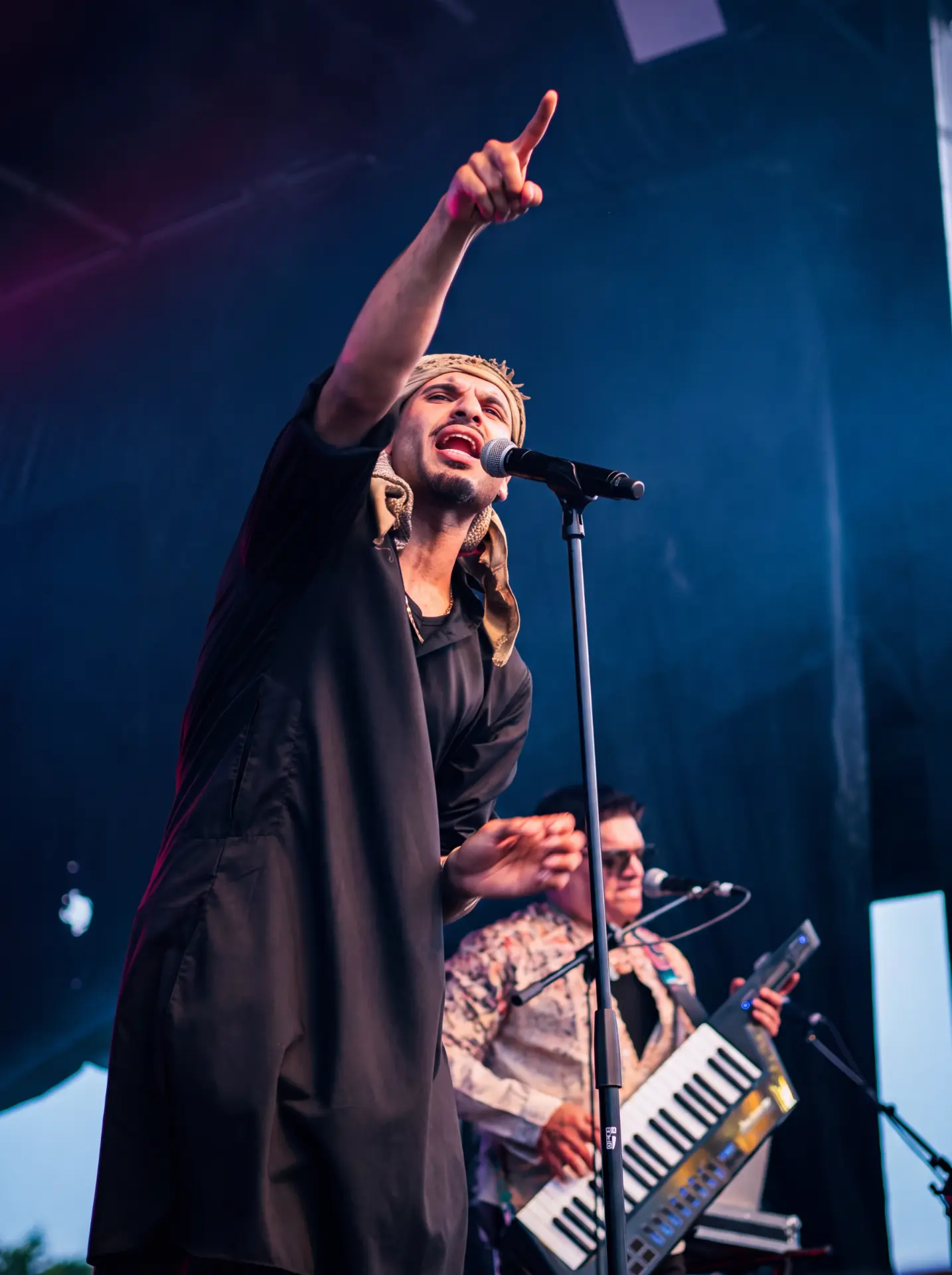 Singer in a headwrap pointing to the sky with a keyboardist behind