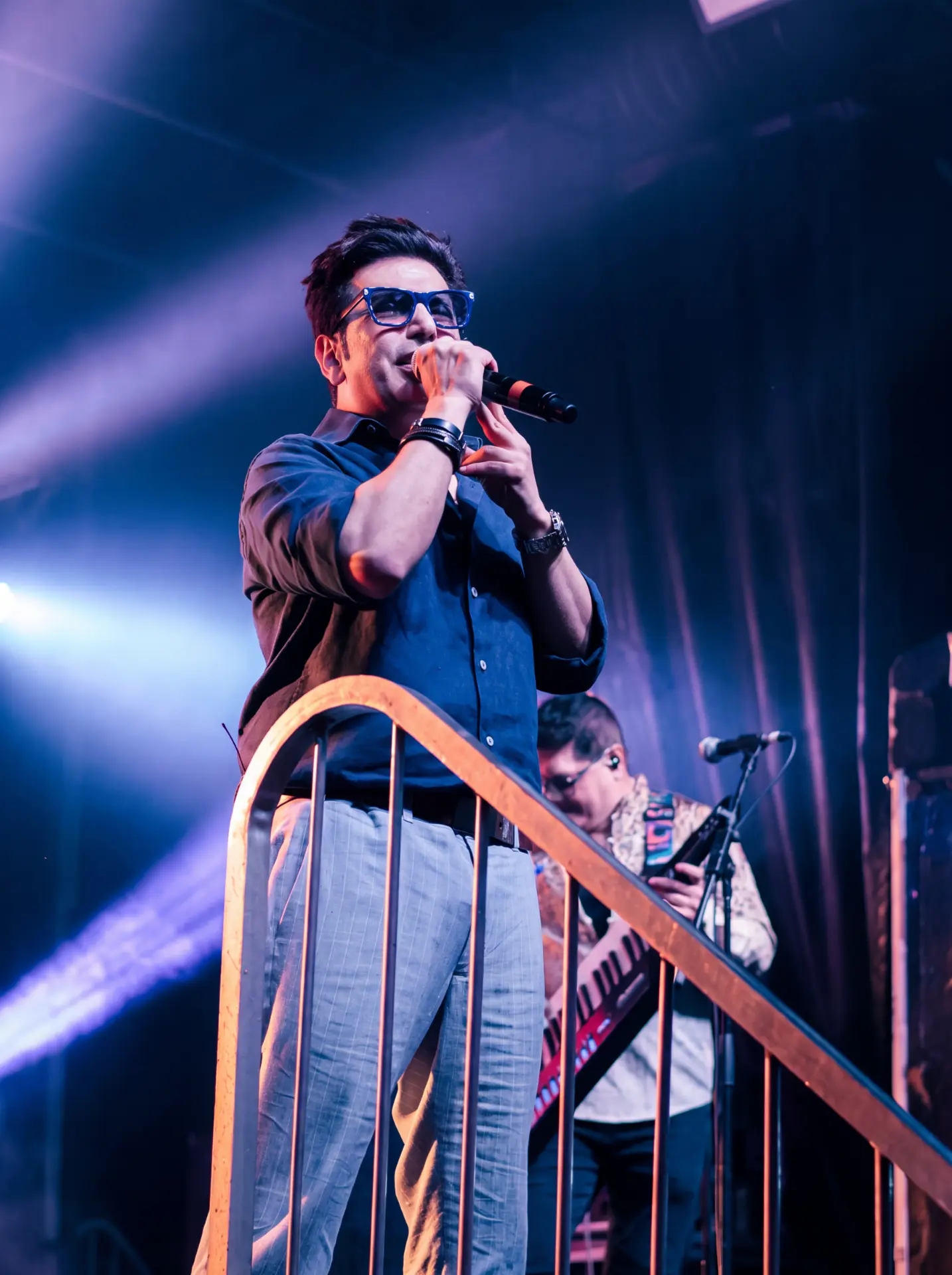 Singer in blue glasses performing behind a stage railing