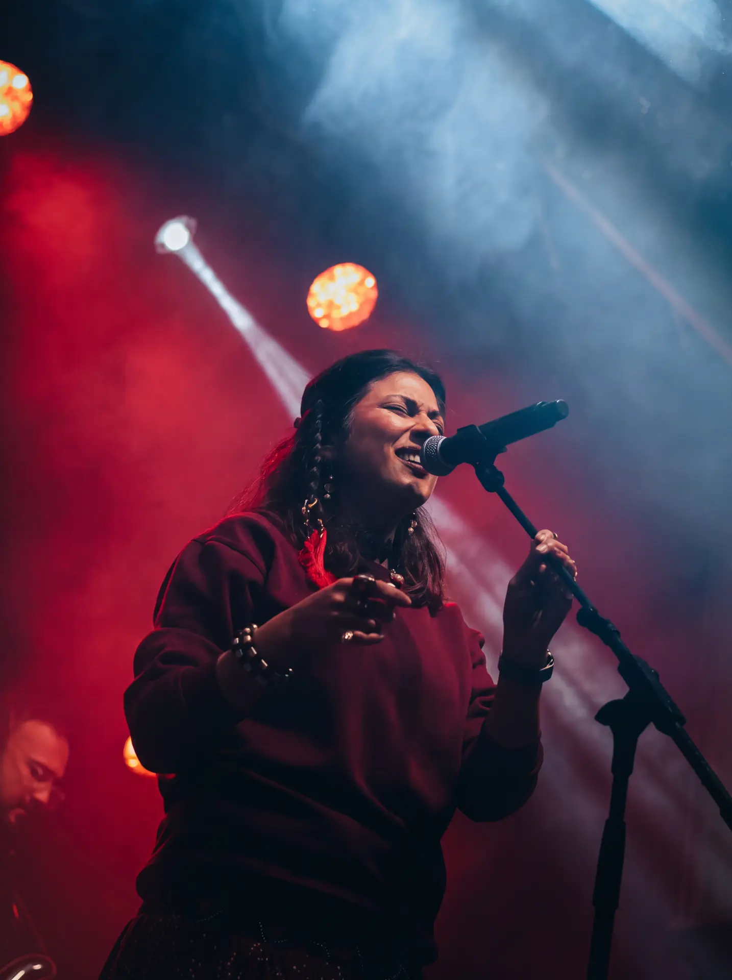 Vocalist gripping the mic stand under warm red lighting